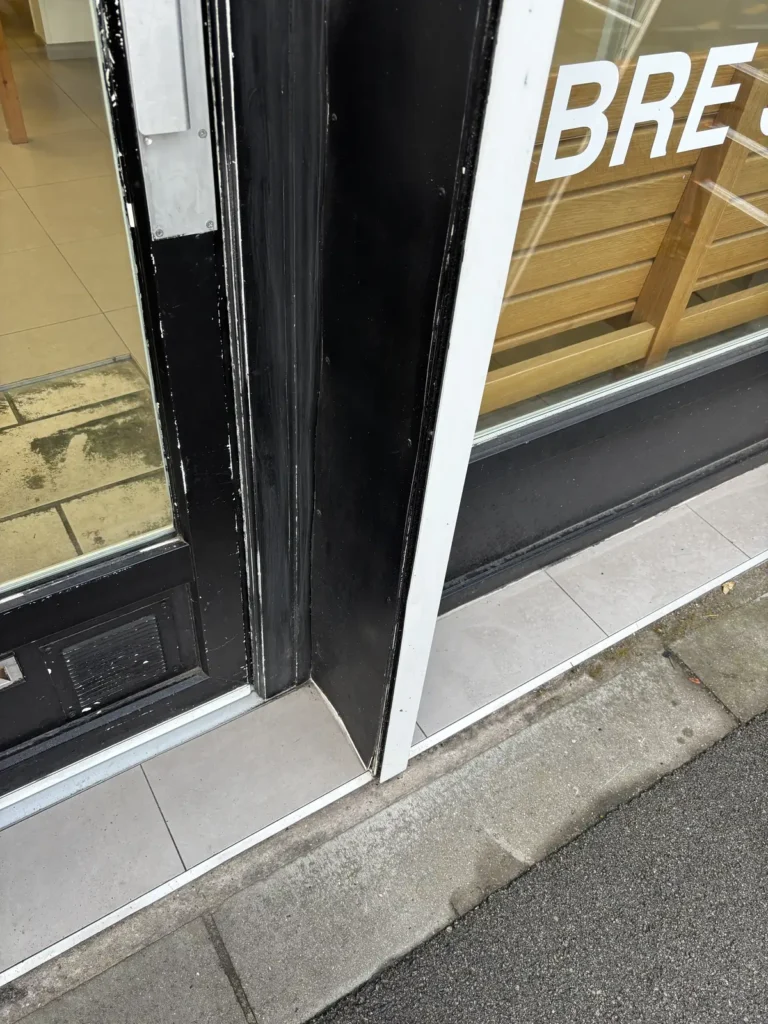Chant de la porte d’entrée de la laverie avec peinture écaillée et plaque PVC déformée avant rénovation